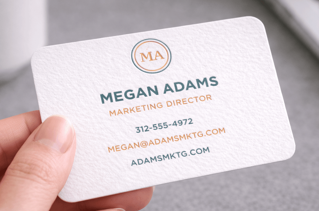 Hand holding a 20pt white cotton letterpress business card with copper foil stamping and rounded corners