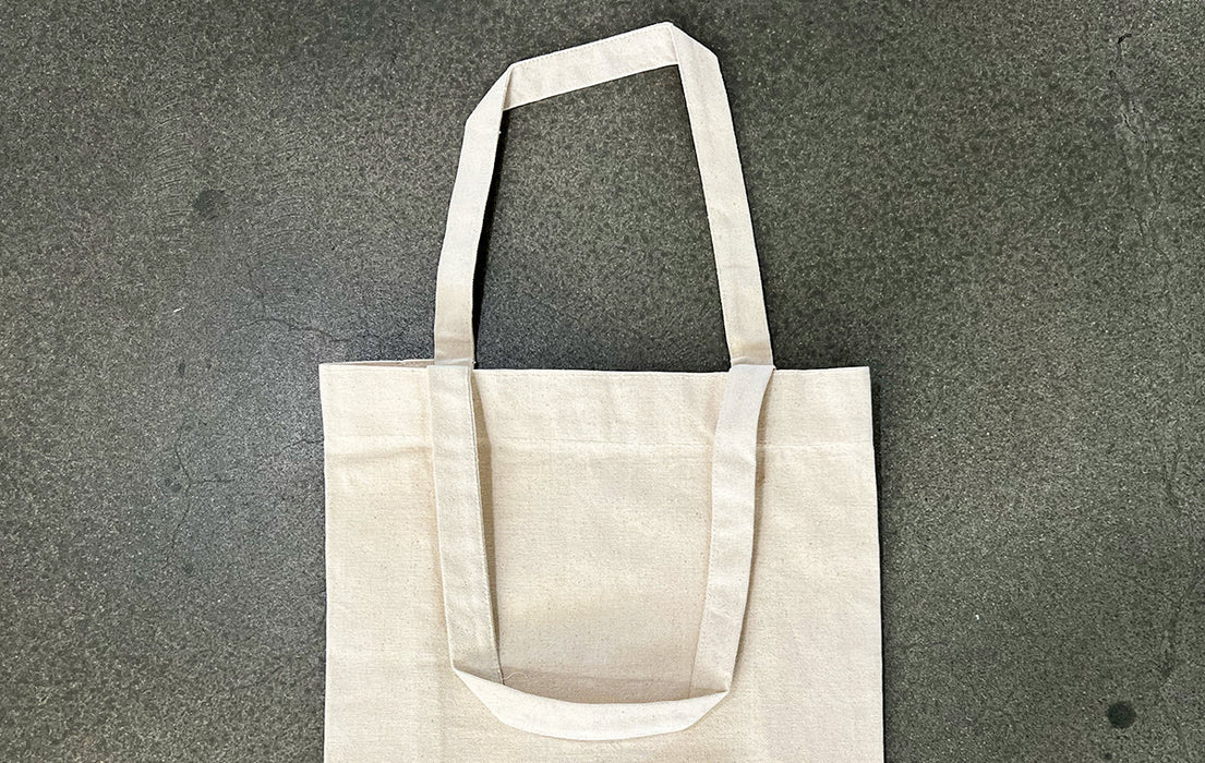 Blank natural cotton tote bag with gusset resting flat on a grey concrete surface