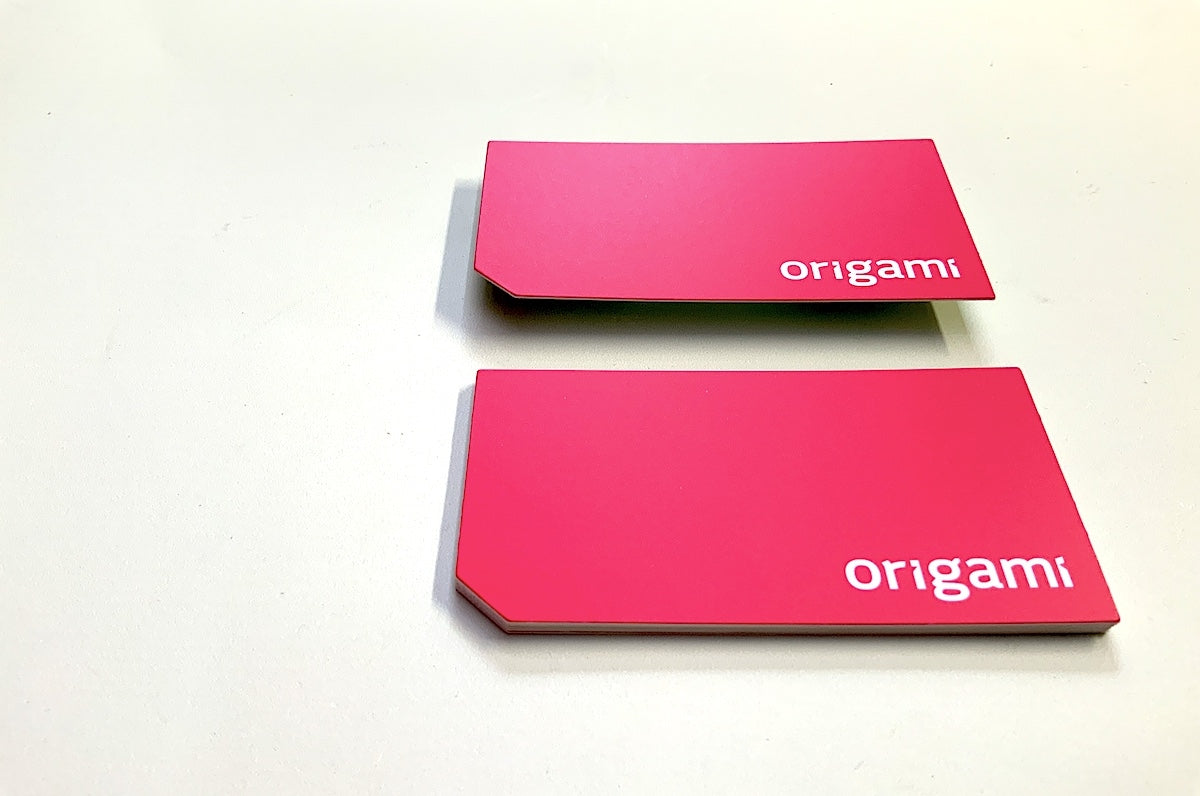 Die cut business cards for Origami on 32pt uncoated stock | pink background with origami in white in the bottom right corner | bottom left corner is cut at a 45 degree angle | Clubcard Printing USA