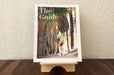 Birch Plywood book display stand holding Palm Springs Life's publication The Guide on a wooden table.